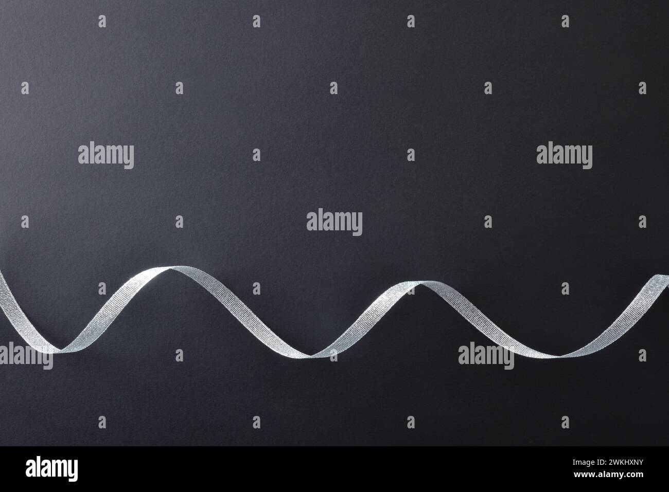 Sfondo scuro a gradiente con nastro in argento lucido ondulato sul fondo per gli eventi. Vista dall'alto. Foto Stock