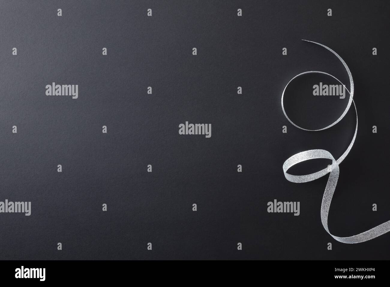 Sfondo da festa sfumato scuro con nastro in argento lucido arricciato sulla destra. Vista dall'alto. Foto Stock