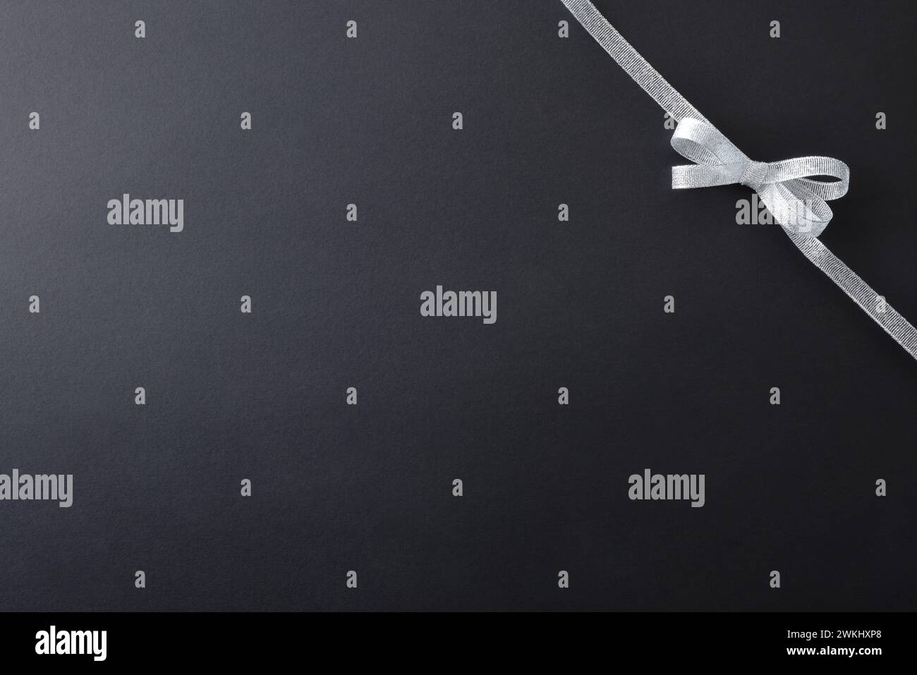 Sfondo sfumato scuro con fiocco argento lucido con nastro nell'angolo superiore destro per gli eventi. Vista dall'alto. Foto Stock
