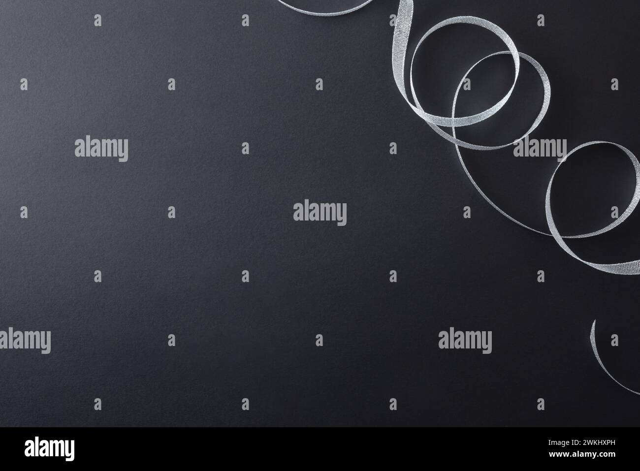 Sfondo sfumato scuro con nastro in argento lucido arricciato nell'angolo superiore destro per gli eventi. Vista dall'alto. Foto Stock