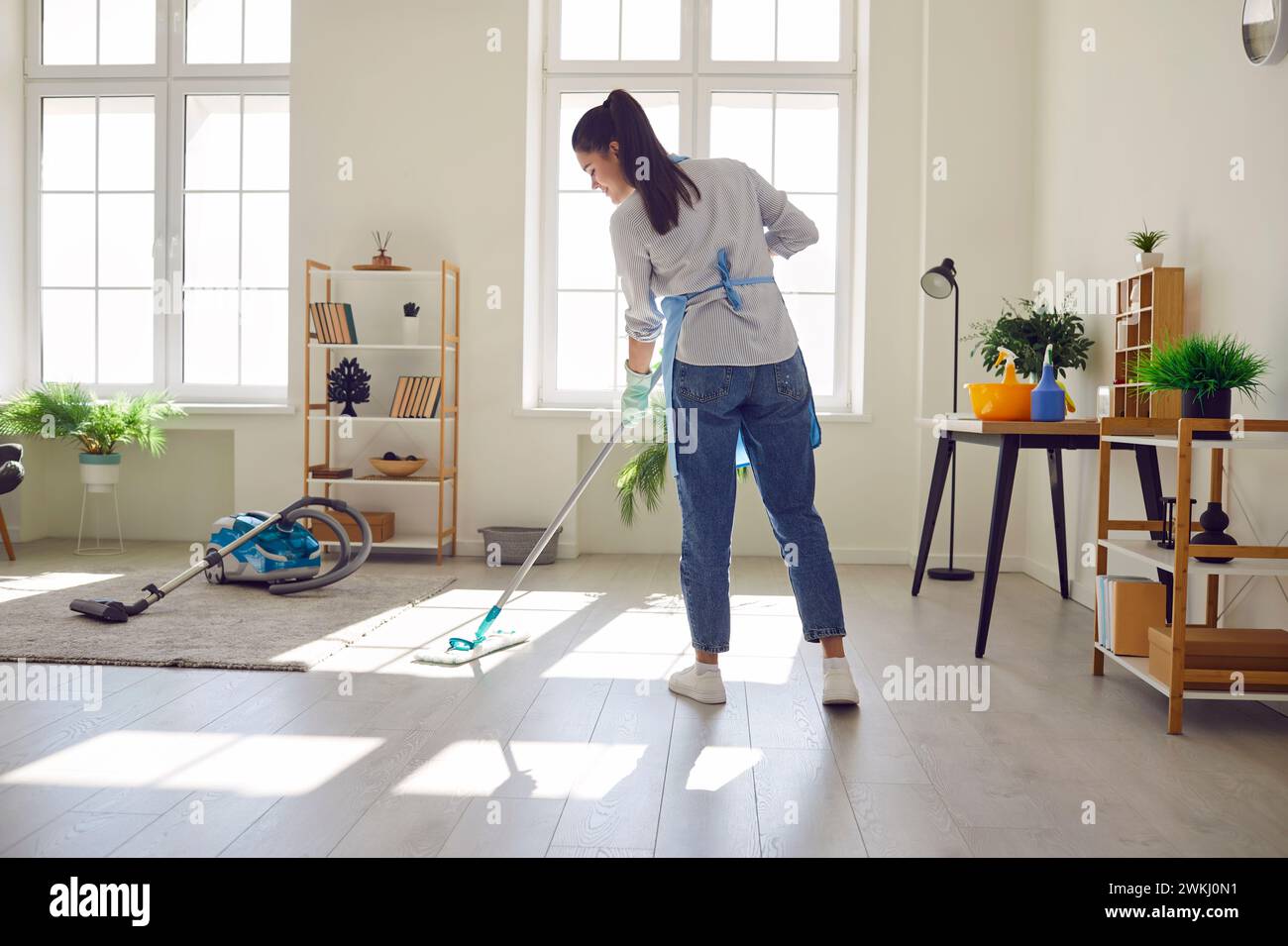 Una giovane donna sorridente casalinga che pulisce il pavimento nel salotto di casa Foto Stock