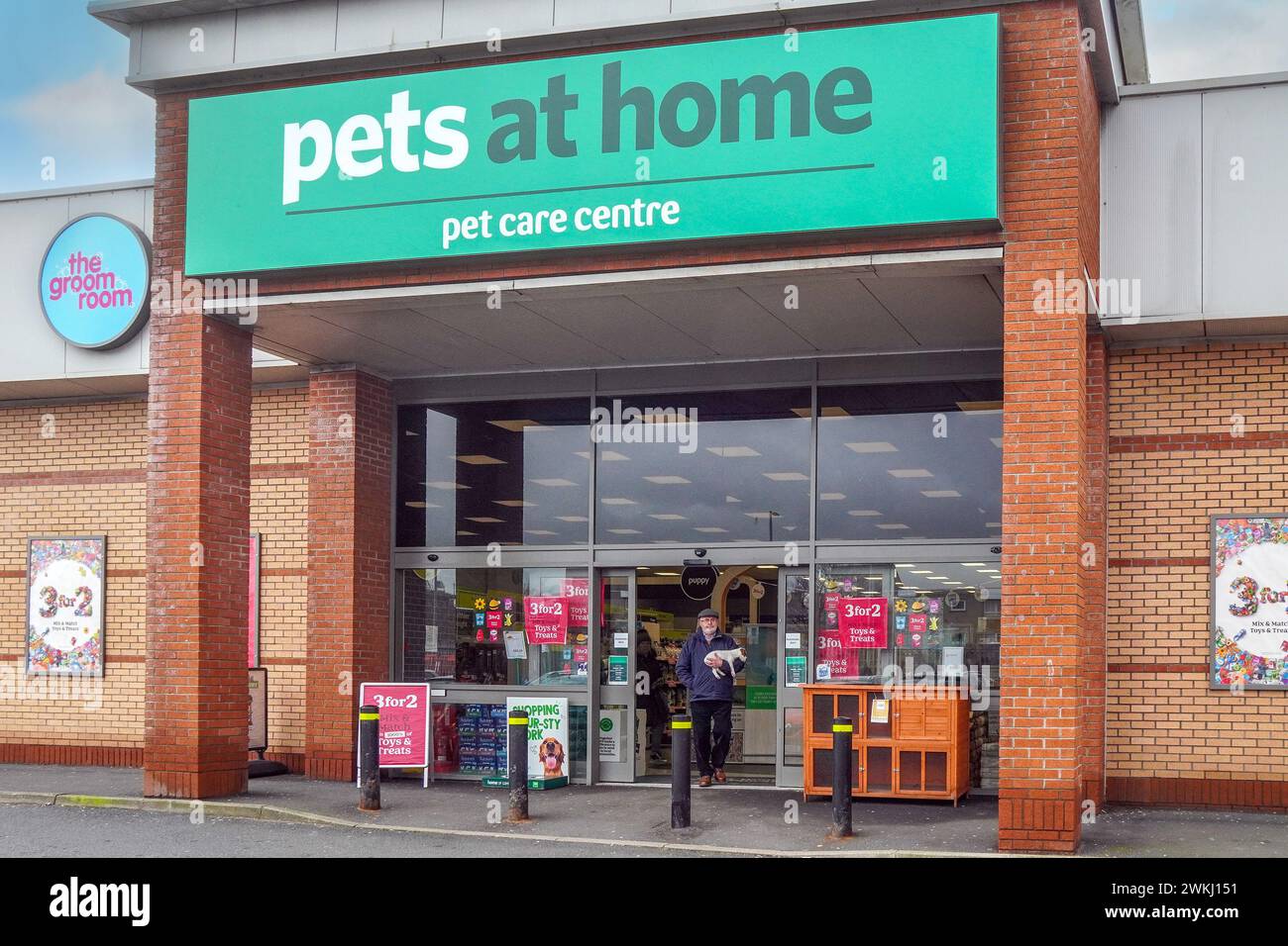Uomo che tiene in mano il cane mentre si trova davanti alla porta del fornitore di animali domestici, Pets at Home, Ayr, Regno Unito Foto Stock