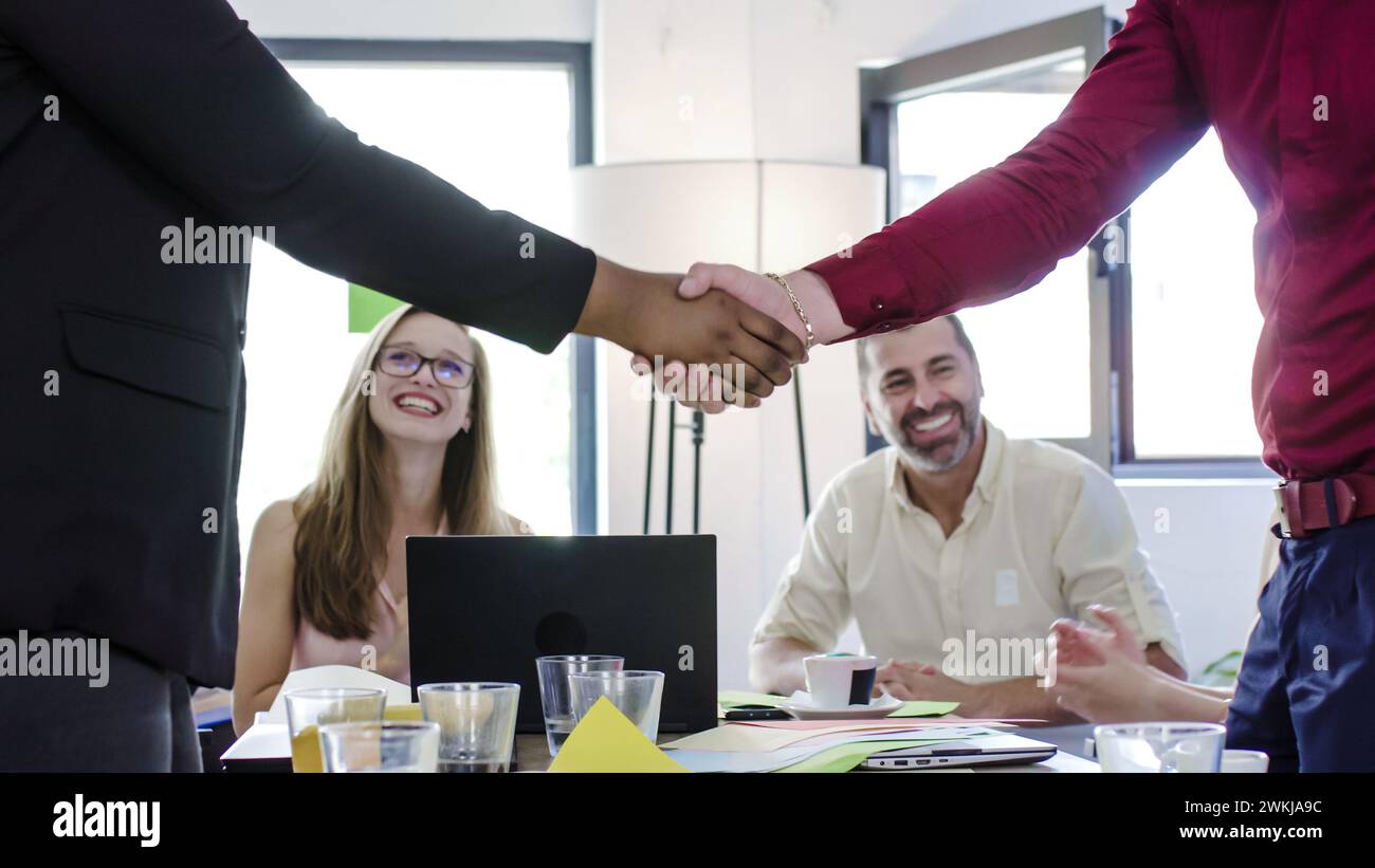 Un gruppo di persone sedute intorno a un tavolo che si stringono di mano come una forma di saluto o di accordo. Colleghi d'affari diversi. Foto Stock