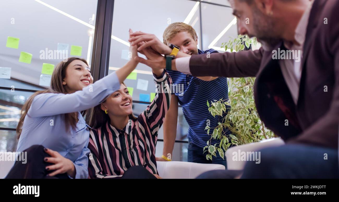 I colleghi d'affari fanno cinque gesti per celebrare il successo. Un gruppo eterogeneo di persone sedute a stretto contatto su un grande divano Foto Stock