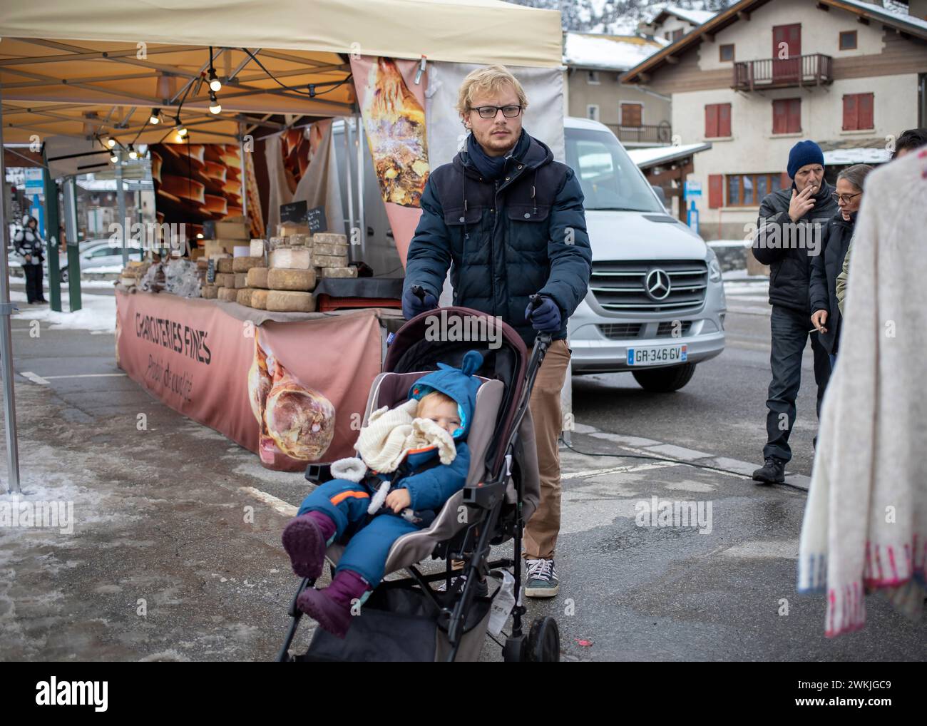 Lanslevillard, Francia, 10 gennaio 2024: Giovane padre con un bambino in un passeggino che cammina al mercato Foto Stock
