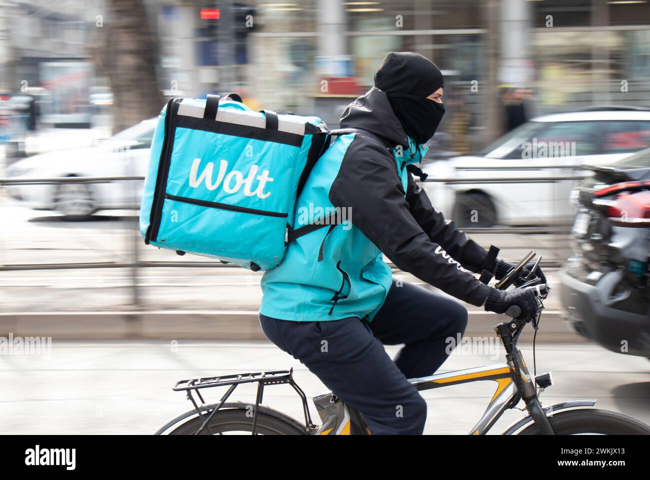 Belgrado, Serbia - 20 febbraio 2024: Servizio di corriere Wolt con una borsa di consegna in bicicletta in una strada trafficata piena di pedoni, vista profilo Foto Stock