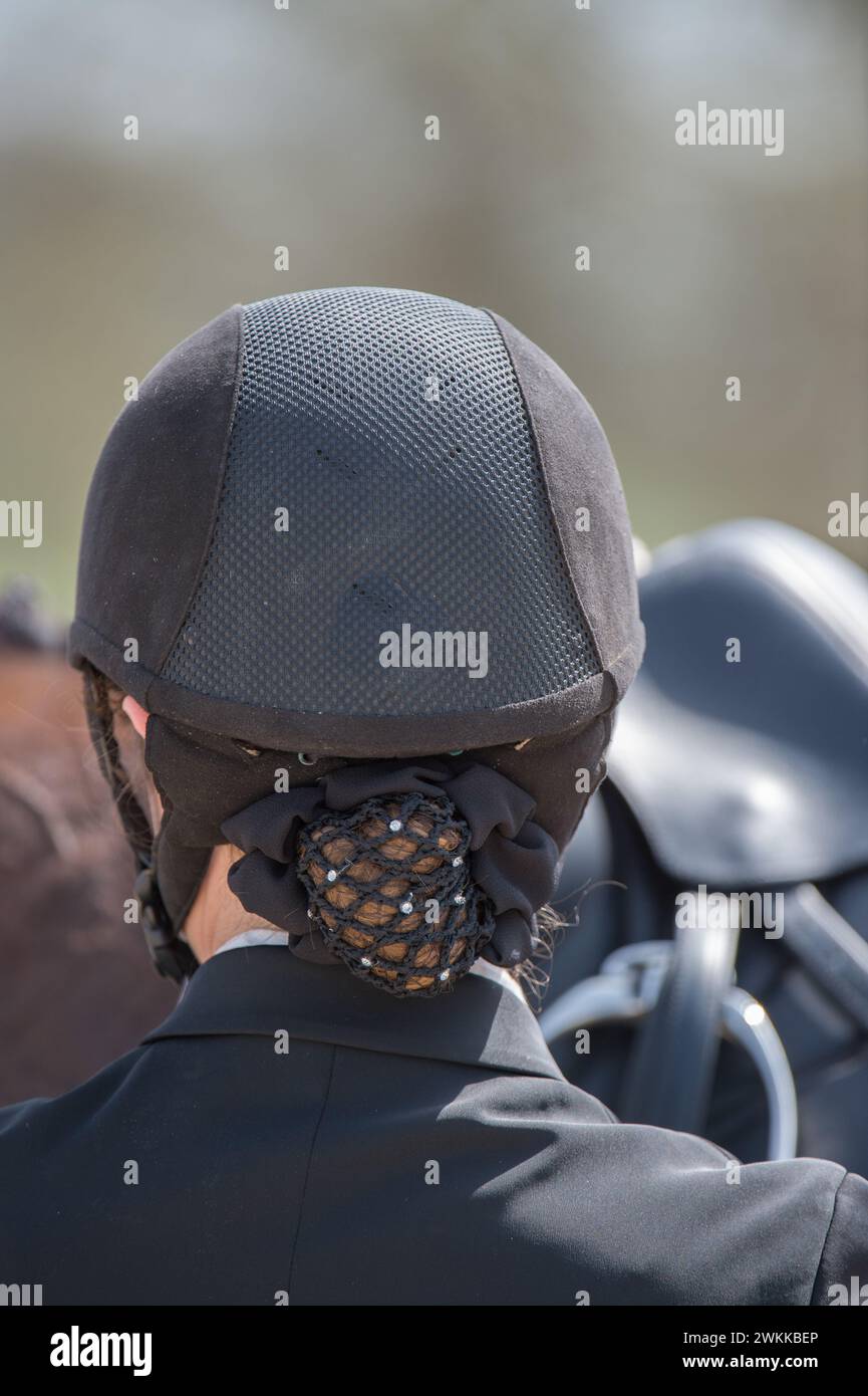 primo piano sul dorso del casco da equitazione su una donna i cui capelli si alzano in rete per capelli equipaggiamento di protezione per l'equitazione per le competizioni ippiche Foto Stock