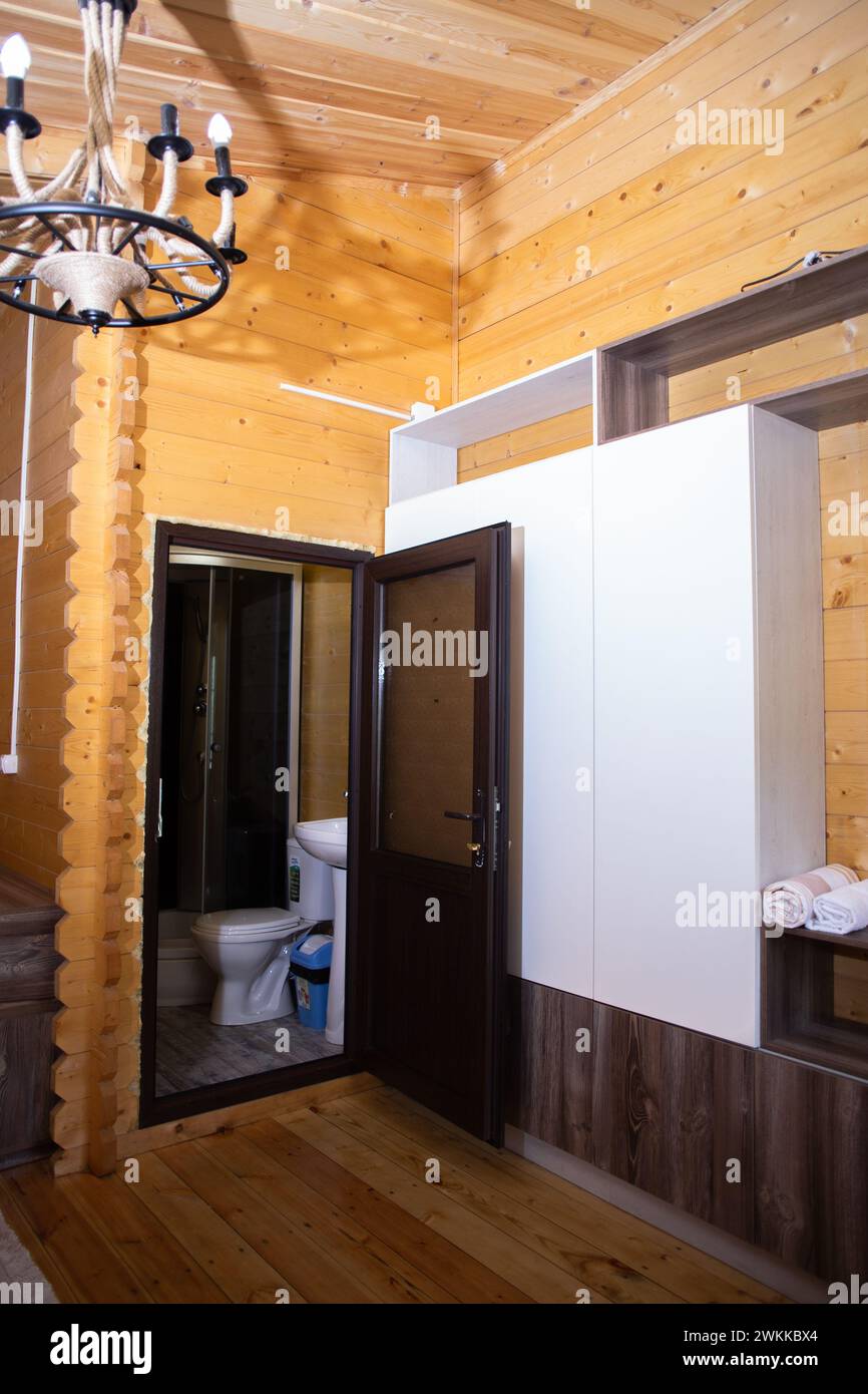 Bagno in casa in legno con doccia ad angolo, WC, lavandino. Porta in vetro, pavimento in legno. Design accogliente, moderno e rustico. Foto Stock