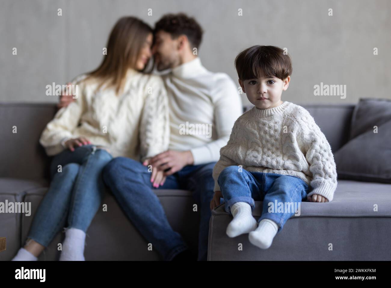 Ridendo felice e giovane famiglia che posa insieme nel soggiorno con un adorabile ragazzo con i denti anteriori mancanti affiancato dal suo sorriso attraente Foto Stock