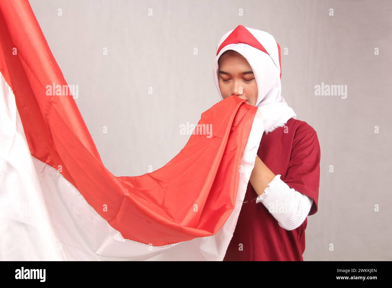 ritratto di donna asiatica hijab che bacia bandiera rossa e bianca indonesiana su sfondo bianco Foto Stock