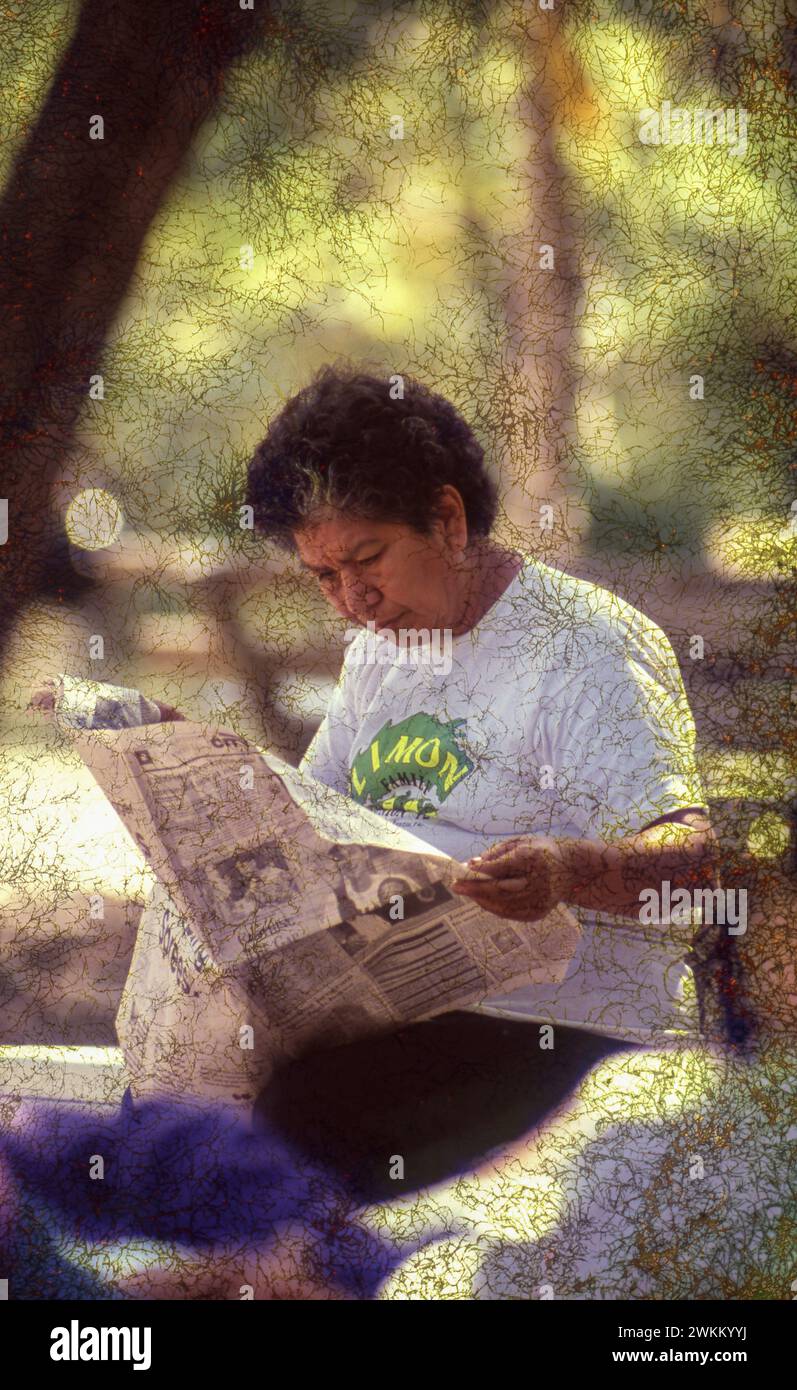 Una donna ispanica legge un giornale nel parco pubblico. ©Bob Daemmrich Foto Stock