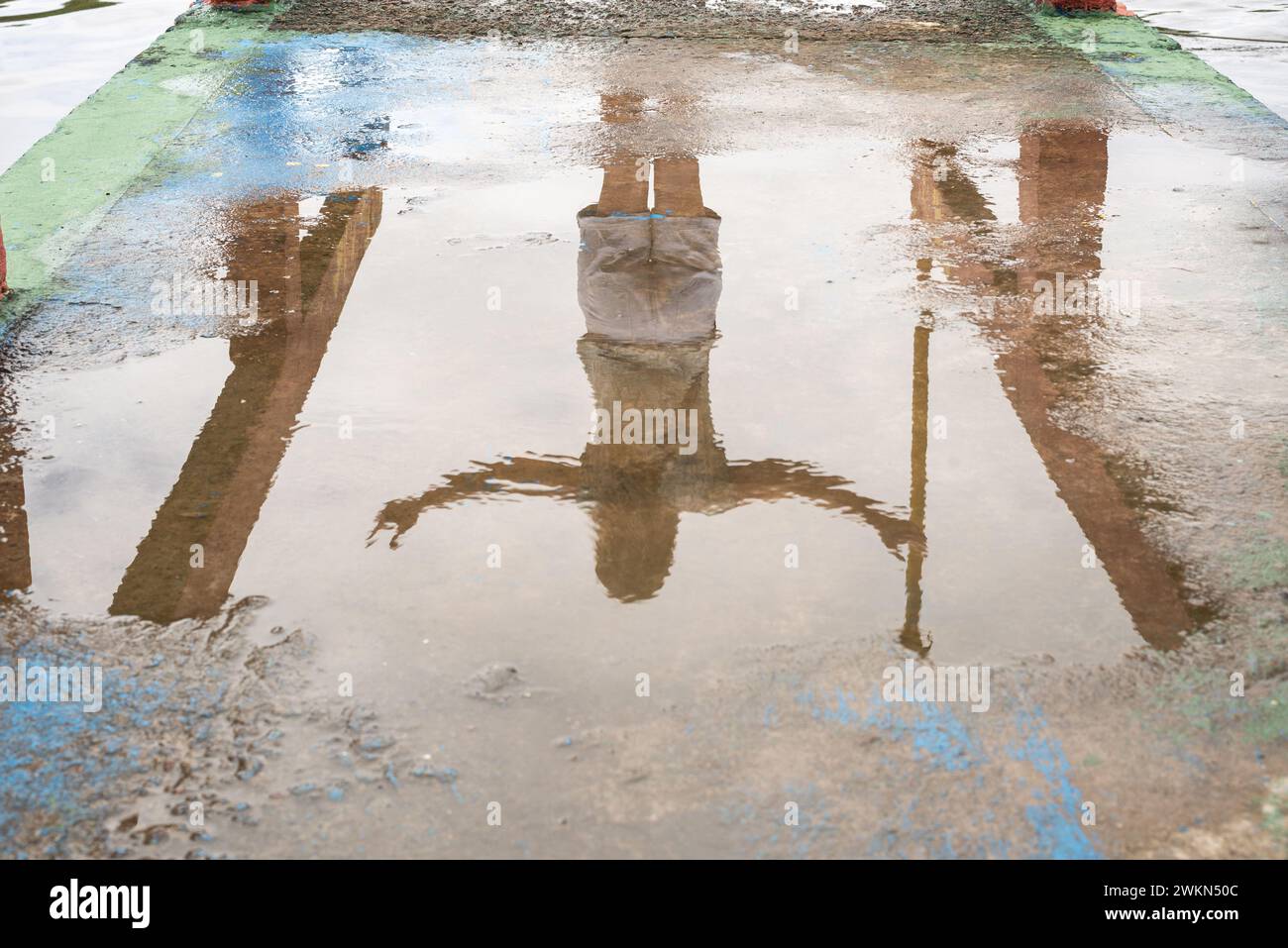 Riflesso di una persona non identificata nella pozzanghera di acqua sul pavimento in cemento. Foto astratte, sfondo e texture. Foto Stock