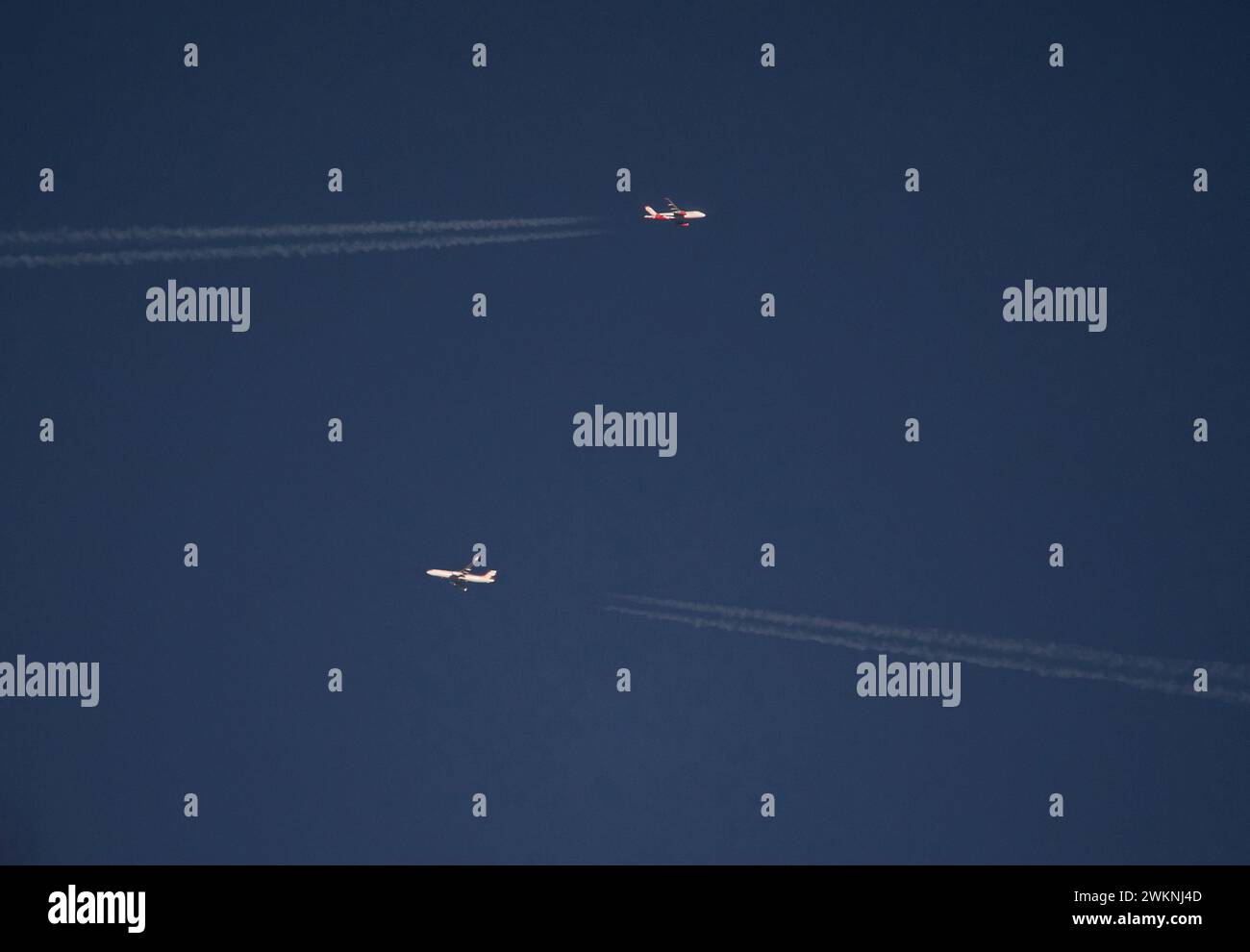 Due aerei di linea passeggeri si passano a vicenda ad alta quota in un cielo blu profondo al tramonto. Foto Stock