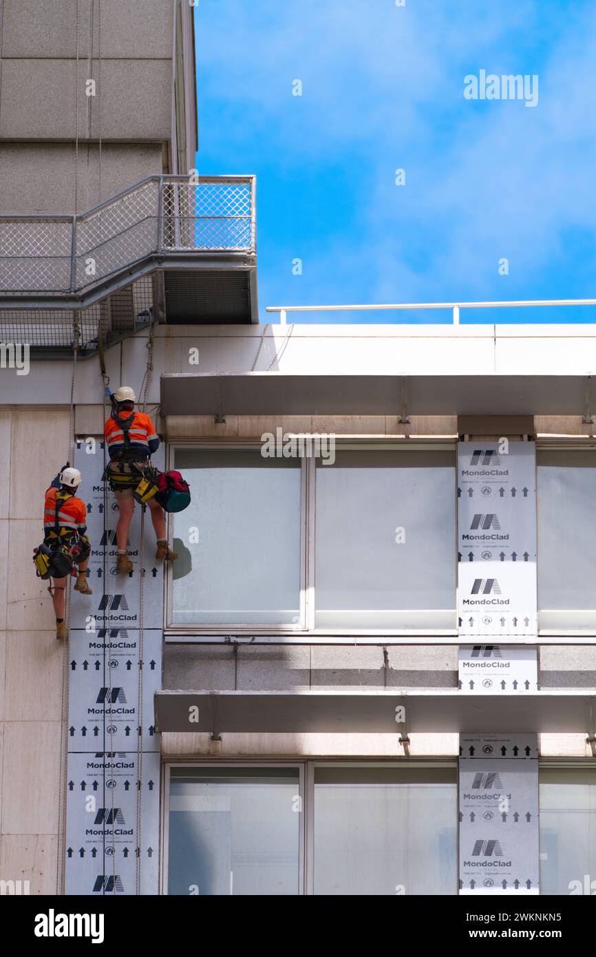 Due uomini che si arrampicano su un edificio per lavori di costruzione, vista esterna, giorno con cielo blu, Melbourne, Australia. Foto Stock