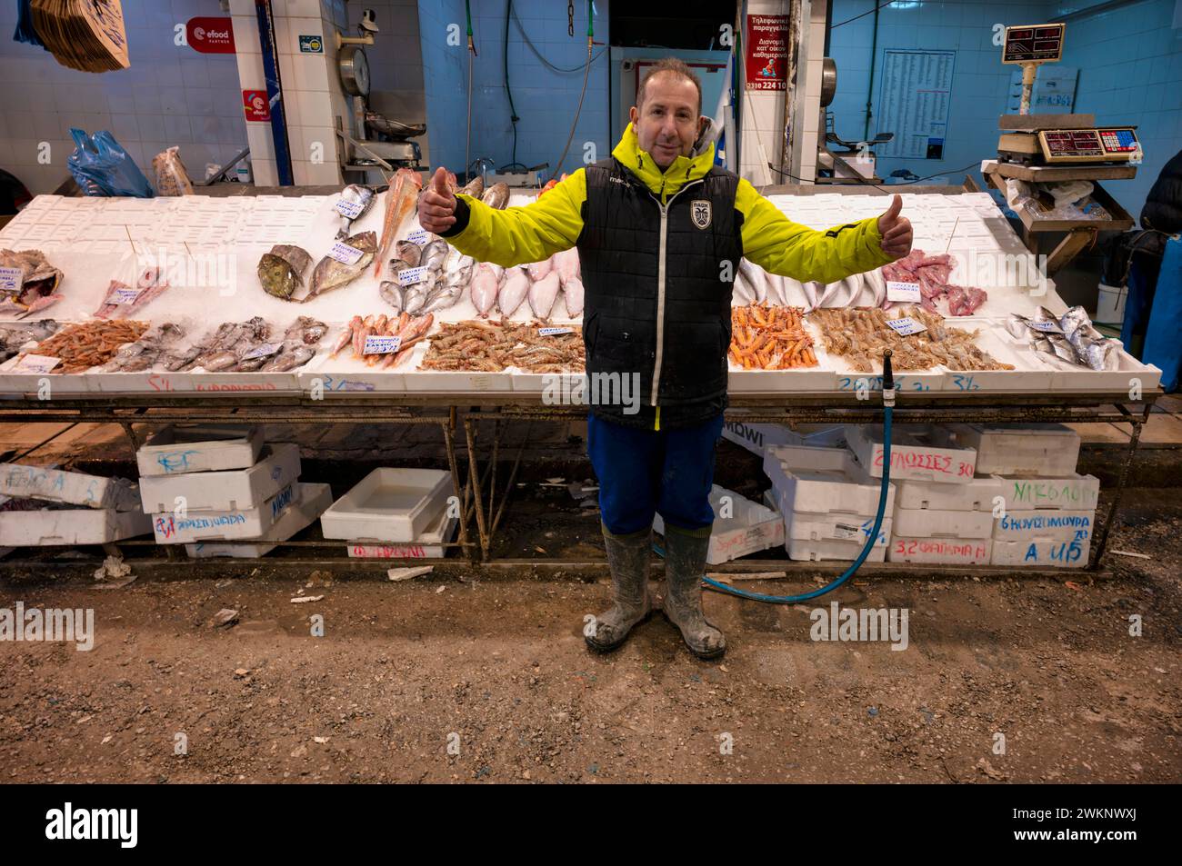 Commerciante, pescivendolo che posa orgogliosamente di fronte al suo bancone del mercato, mostra di pesce fresco e frutti di mare sul ghiaccio, cibo, mercato Kapani, Vlali, Salonicco Foto Stock