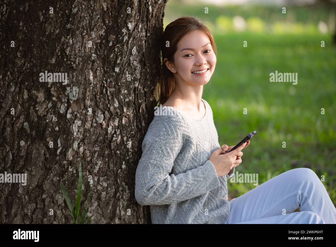 Giovane donna asiatica che usa lo smartphone mentre siede a terra nel parco cittadino. Foto Stock