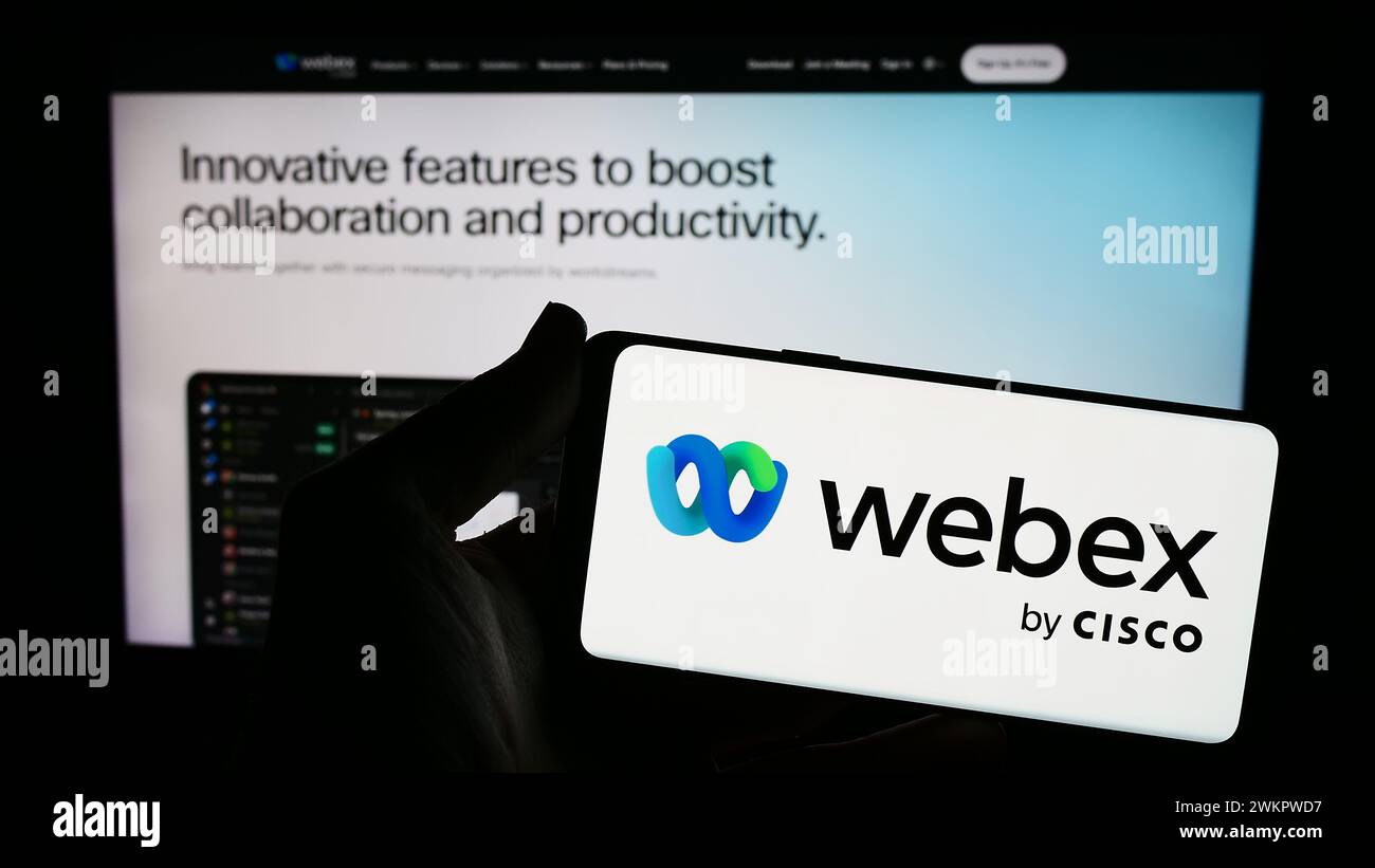 Persona che possiede uno smartphone con il logo della società statunitense di comunicazioni unificate Webex by Cisco davanti al sito Web. Mettere a fuoco il display del telefono. Foto Stock