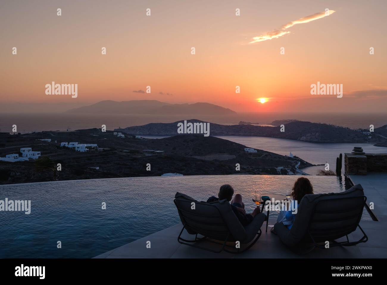 IOS, Grecia - 17 settembre 2023: Veduta di una coppia seduta davanti ad una piscina presso un lounge bar che si gode lo spettacolare tramonto a iOS Grecia Foto Stock