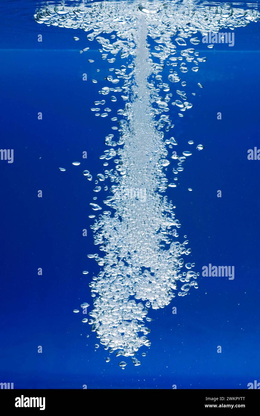un sottile getto d'acqua penetra nella superficie dell'acqua e produce molte bolle d'aria nell'acqua blu di un acquario Foto Stock
