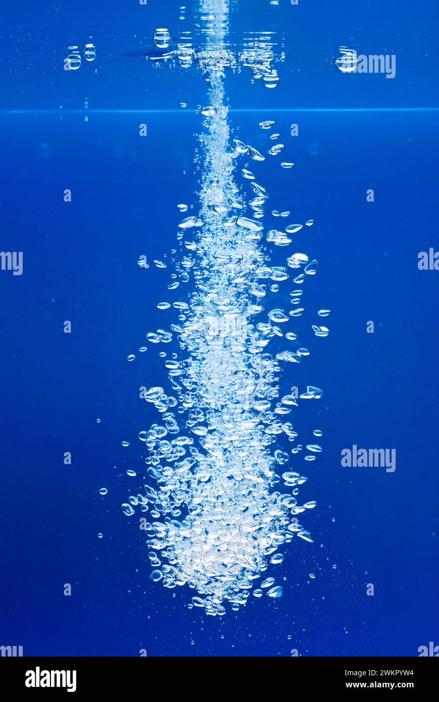 un sottile getto d'acqua penetra nella superficie dell'acqua e produce molte bolle d'aria nell'acqua blu di un acquario Foto Stock