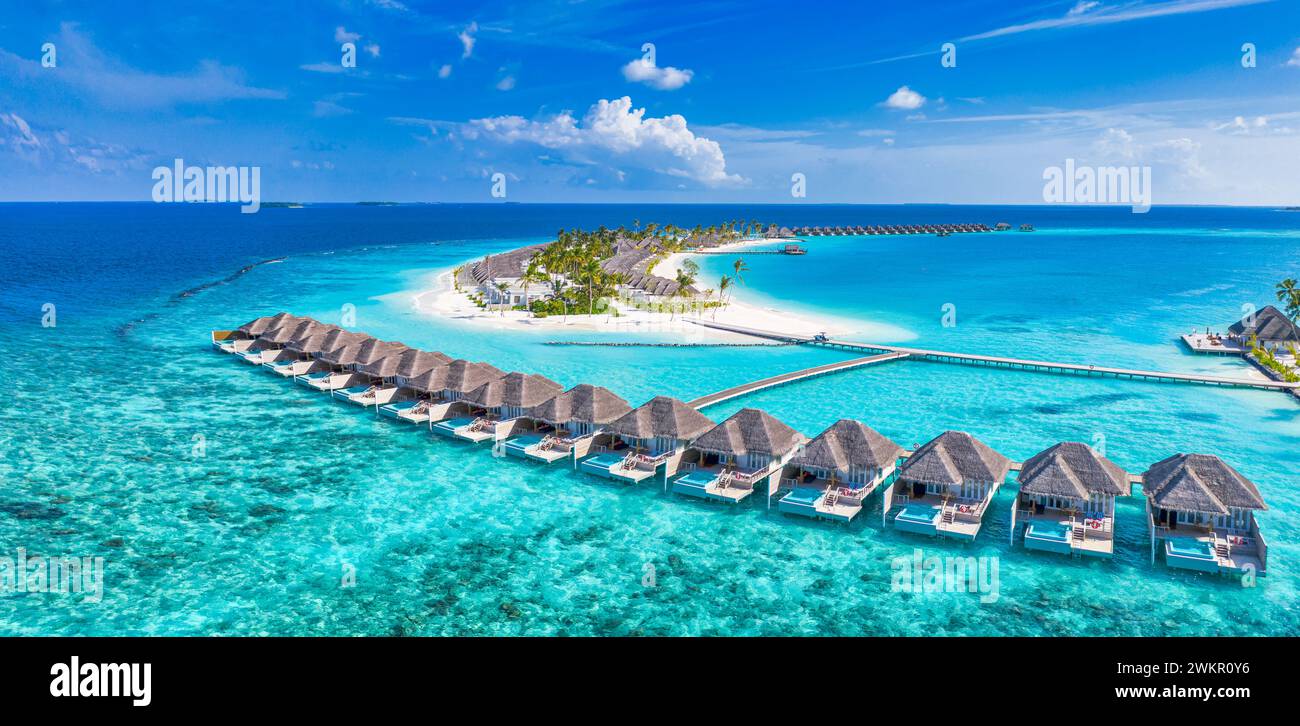 Tranquillo paesaggio aereo, lussuose ville tropicali sull'acqua. Bellissima spiaggia di palme sull'isola cielo soleggiato. Stupendi occhi d'uccello, viste panoramiche delle Maldive Foto Stock