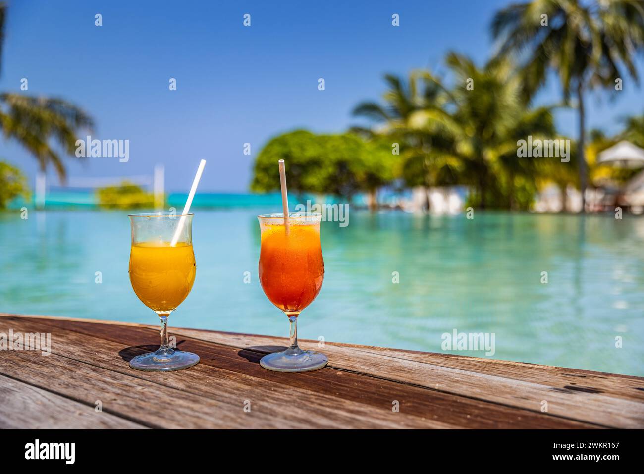 Cocktail colorati serviti in un lussuoso resort tropicale alle Maldive. A bordo piscina con palme e lettini sfocati e luce solare. Giornata di sole Foto Stock