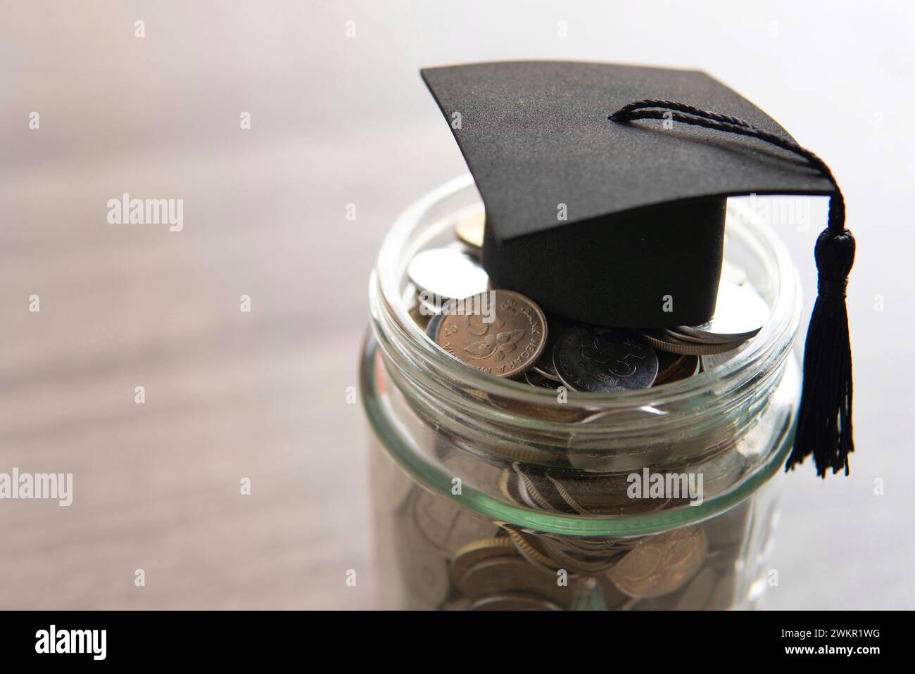 Vaso in vetro riempito di monete e un cappuccio graduato sopra. Copia spazio per il testo. Concetto di risparmio nel settore dell'istruzione. Foto Stock