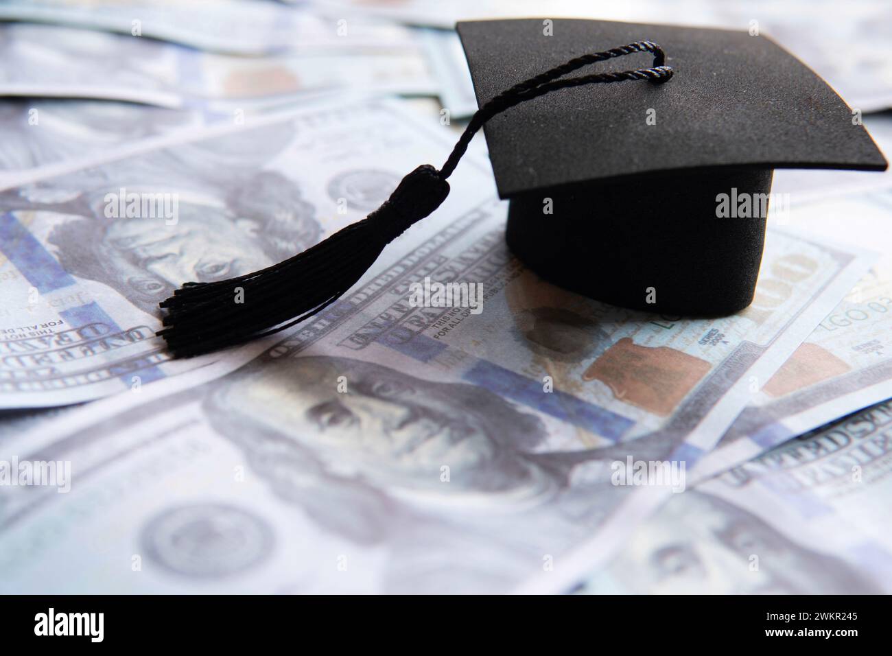 Cappello graduato in cima a una pila di banconote da cento dollari. Finanziamento dell'istruzione, concetto di prestito per studenti. Foto Stock