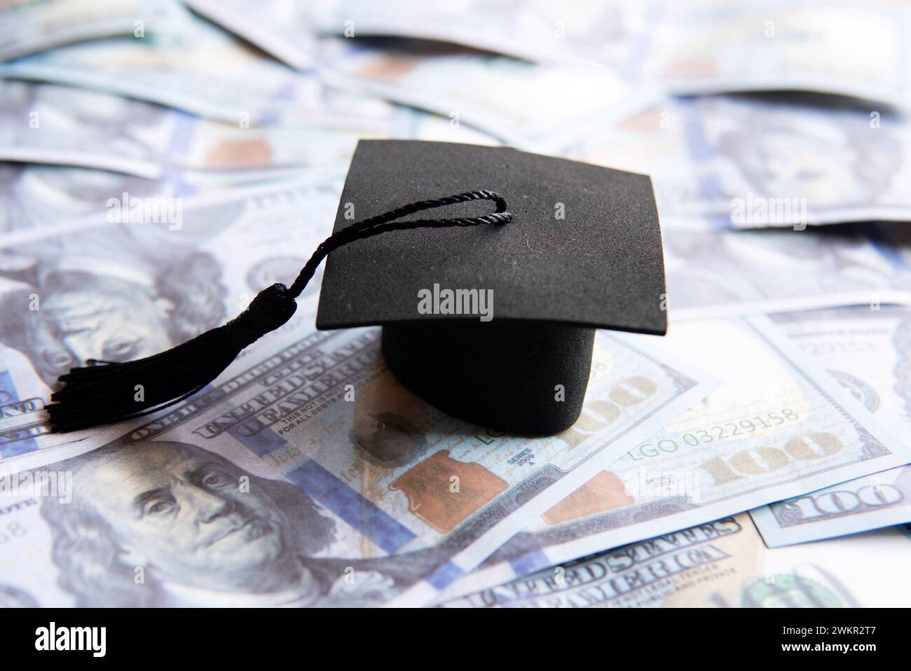 Cappello graduato in cima a una pila di banconote da cento dollari. Finanziamento dell'istruzione, concetto di prestito per studenti. Foto Stock
