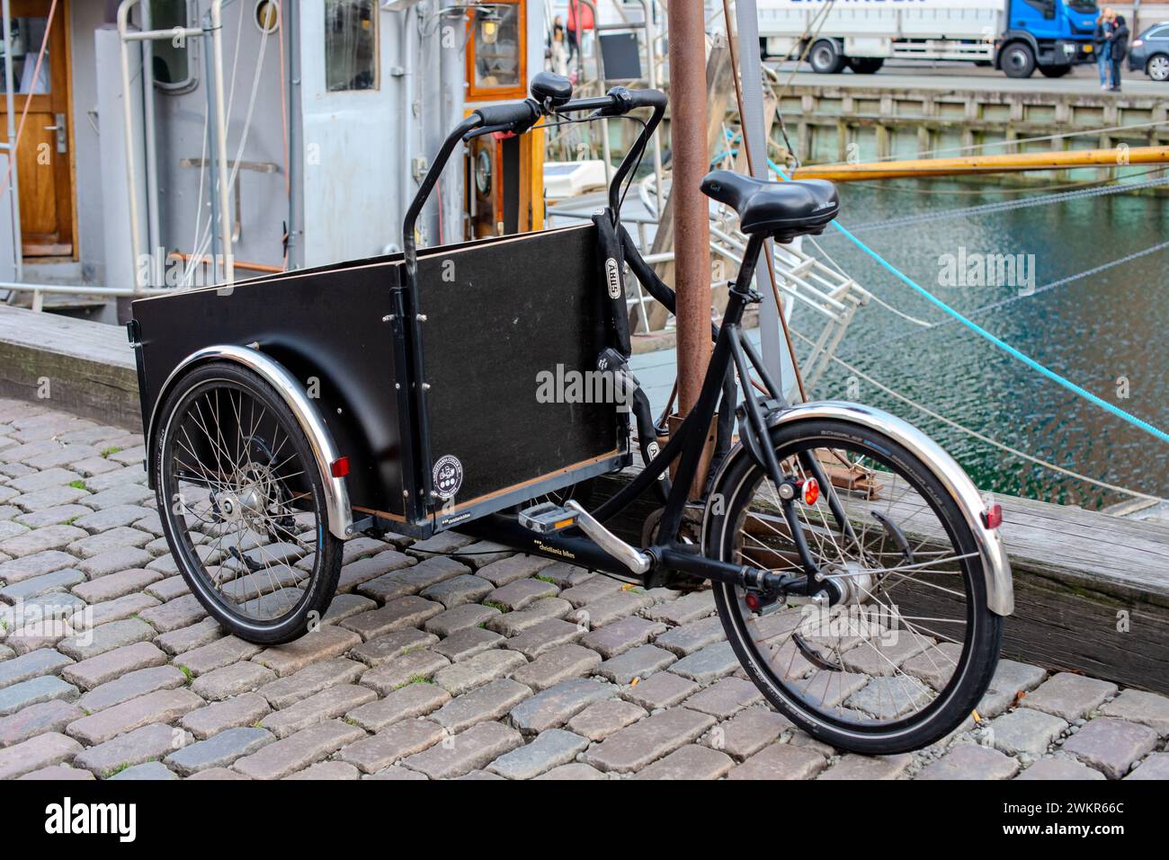 Una bicicletta con rimorchio di carico coperto parcheggiata da una barca. Foto Stock