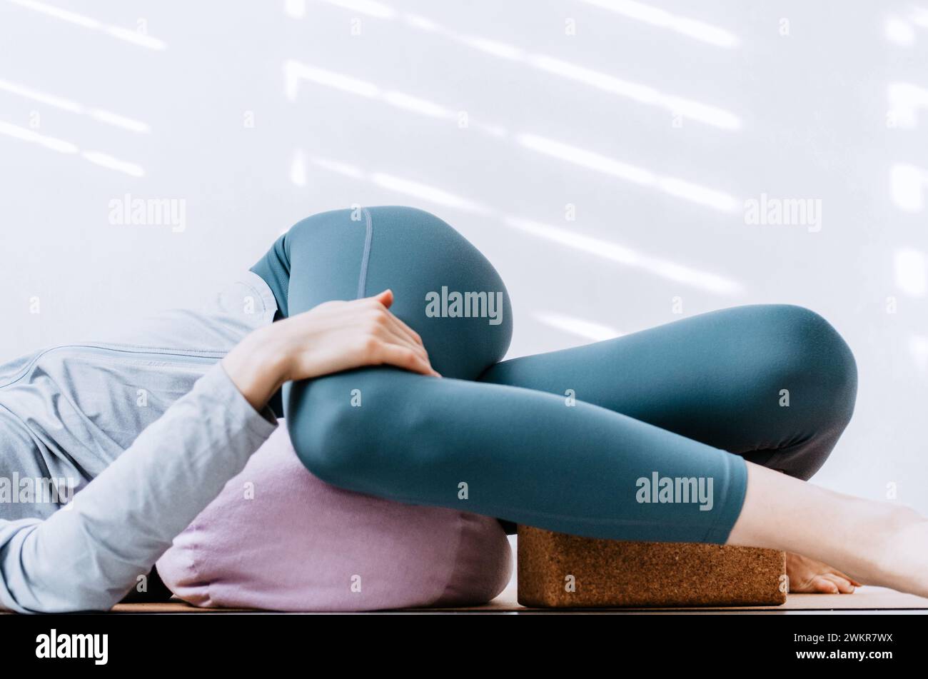 Donna che fa yin yoga torsioni passive supine con sostegno e blocco di sughero Foto Stock