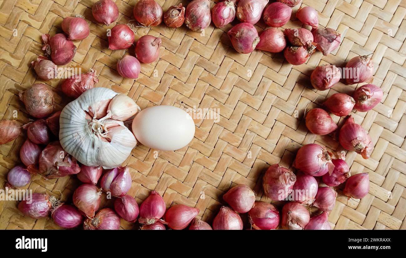 Foto di spezie sotto forma di scalogni, aglio, peperoncini e uova disposte in un bambù intrecciato Foto Stock