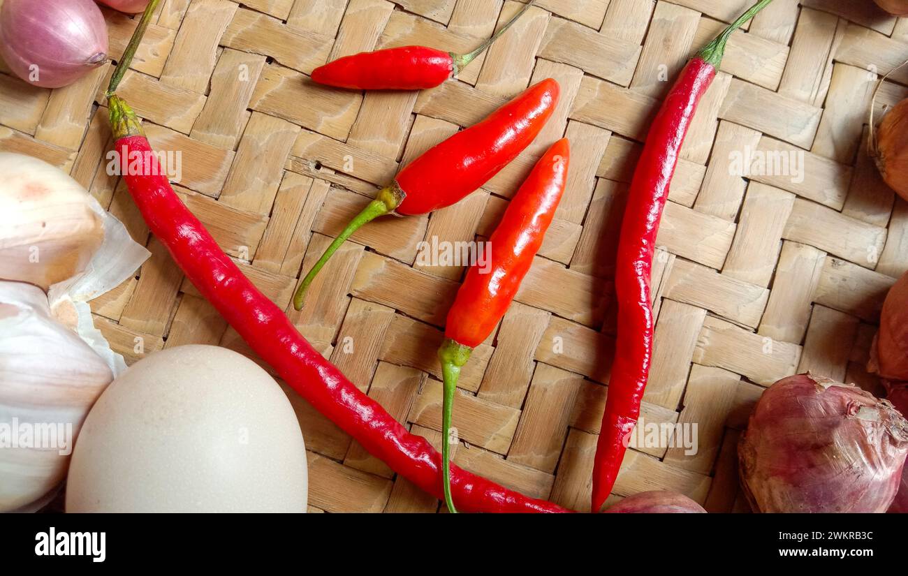 Foto di spezie sotto forma di scalogni, aglio, peperoncini e uova disposte in un bambù intrecciato Foto Stock
