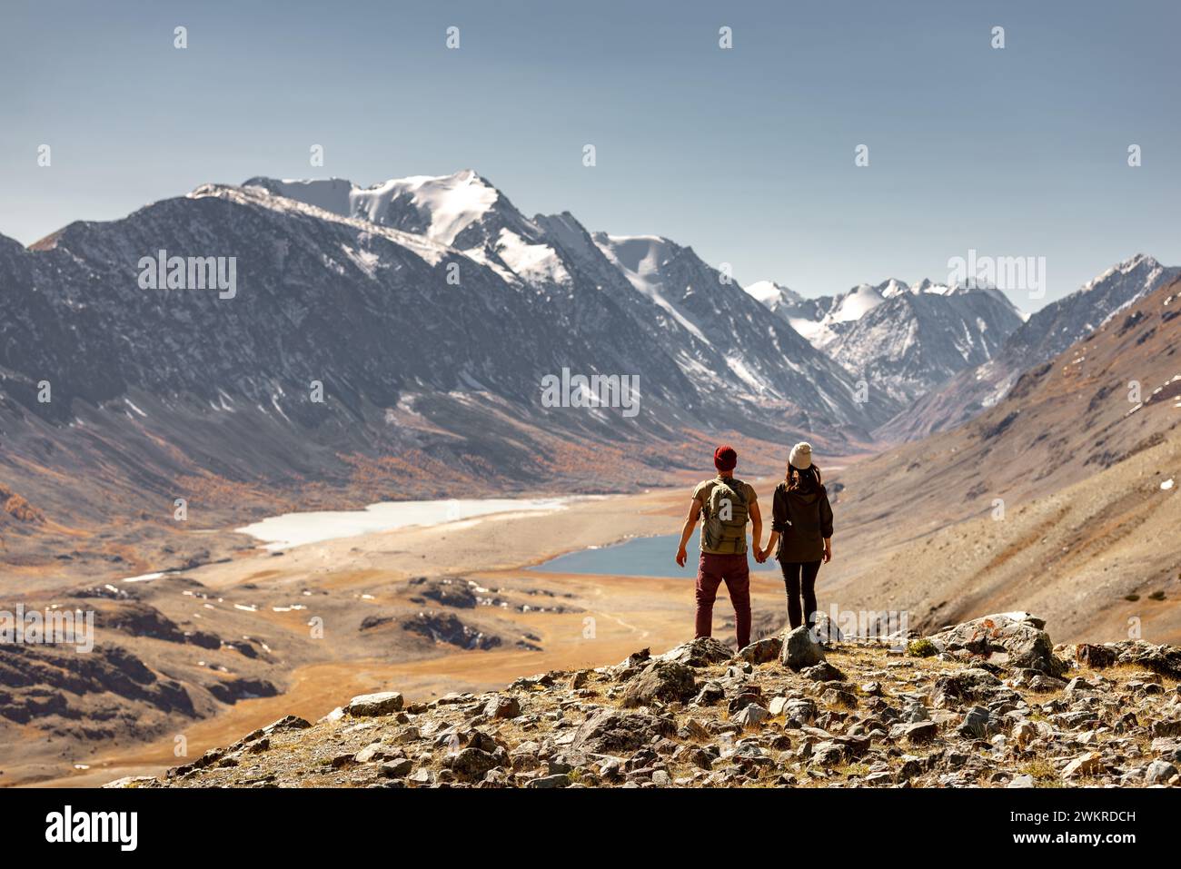 Una coppia di turisti o escursionisti si trova in cima alla montagna e gode di una bella vista sulla valle con due laghi e piccoli ghiacciai Foto Stock