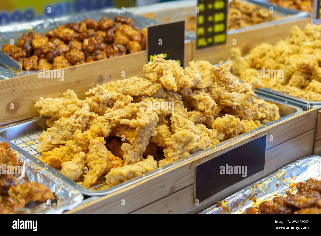 Vassoi pieni di croccanti pezzi di pollo fritto dorato, pronti per essere serviti ai clienti in un mercato alimentare affollato Foto Stock