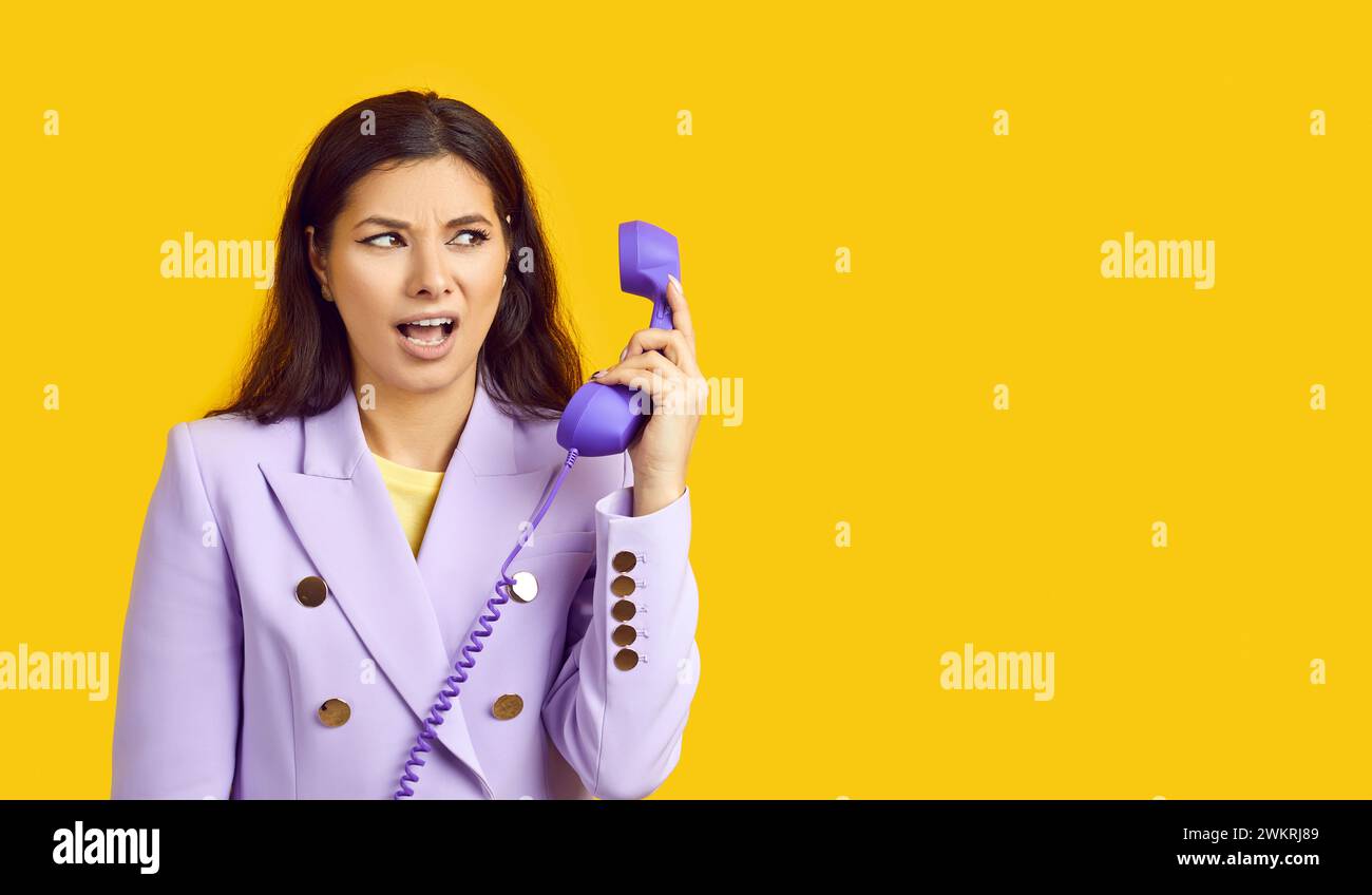 Donna d'affari arrabbiata frustrata dalle conversazioni al telefono fisso, isolata su un muro giallo Foto Stock