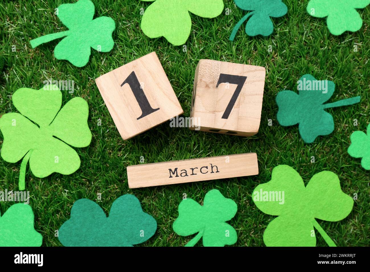St Giorno di Patrick - 17 marzo. Calendario a blocchi di legno e foglie di trifoglio di feltro su erba verde, stesa piatta Foto Stock