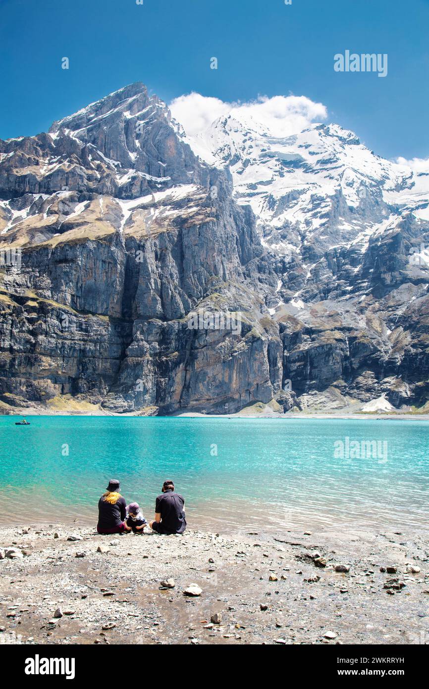 Famiglia che siede ai margini del lago Oeschinen (Oeschinensee) e con il monte Blüemlisalp sullo sfondo, Svizzera Foto Stock