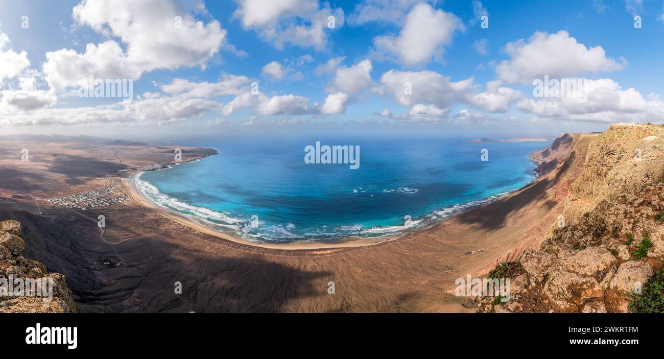 Ampie vedute di Playa Famara, Lanzarote, con le sue sabbie dorate abbracciate da acque azzurre e scogliere spettacolari, un paradiso per i surfisti. Foto Stock