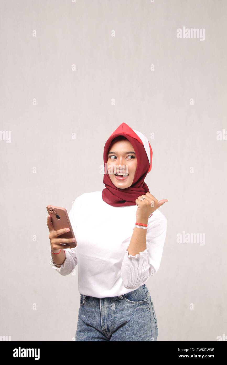 giovane donna asiatica che indossa hijab che tiene il telefono cellulare con il viso sorridente area candida sfondo bianco vuoto, concetto di giorno dell'indipendenza Foto Stock