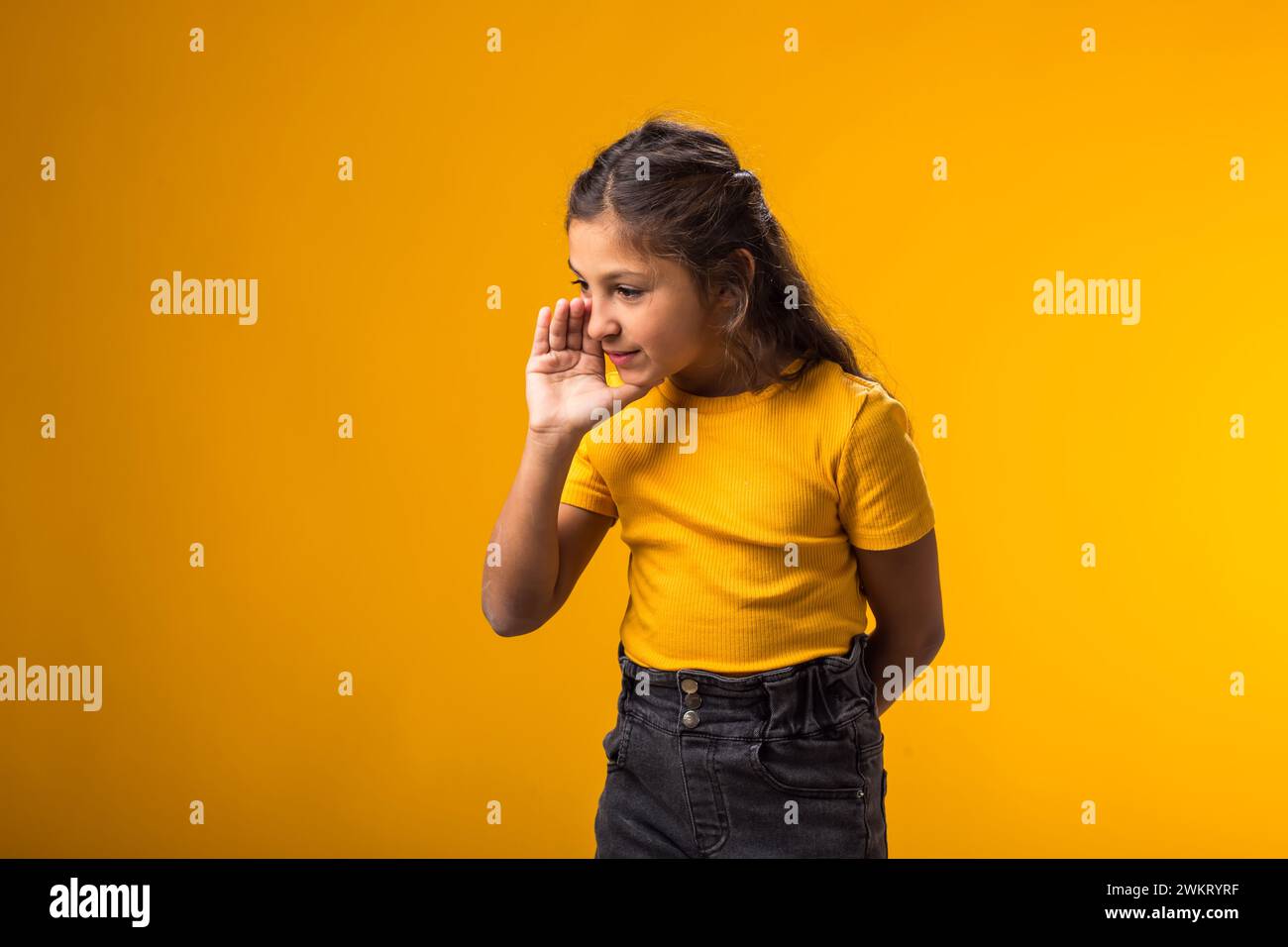 Ritratto di una bambina che urla e tiene il palmo vicino alla bocca aperta. Pettegolezzi e concetto segreto Foto Stock