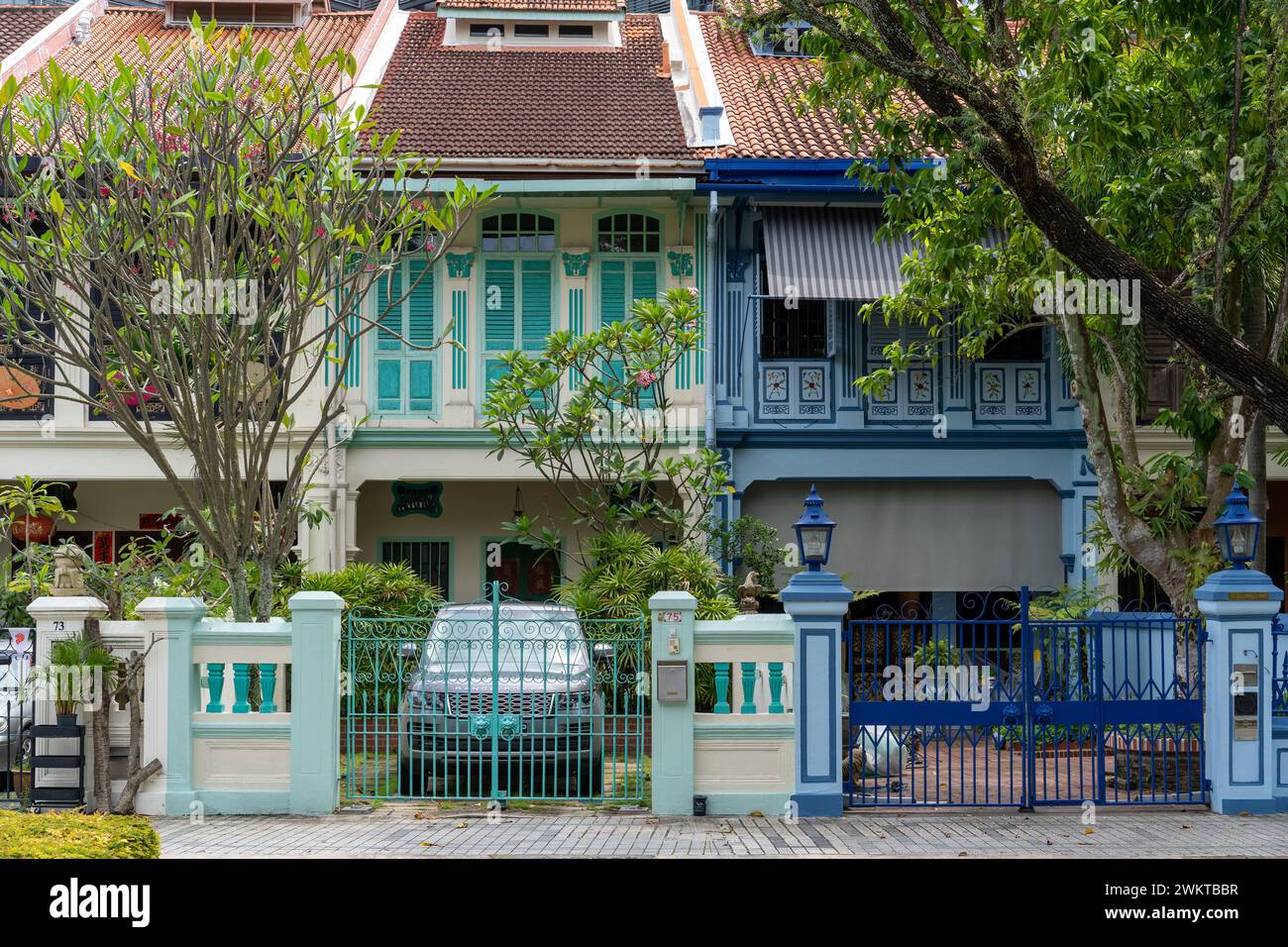 Città vivace con tre case colorate, recinzione blu e cancello Foto Stock