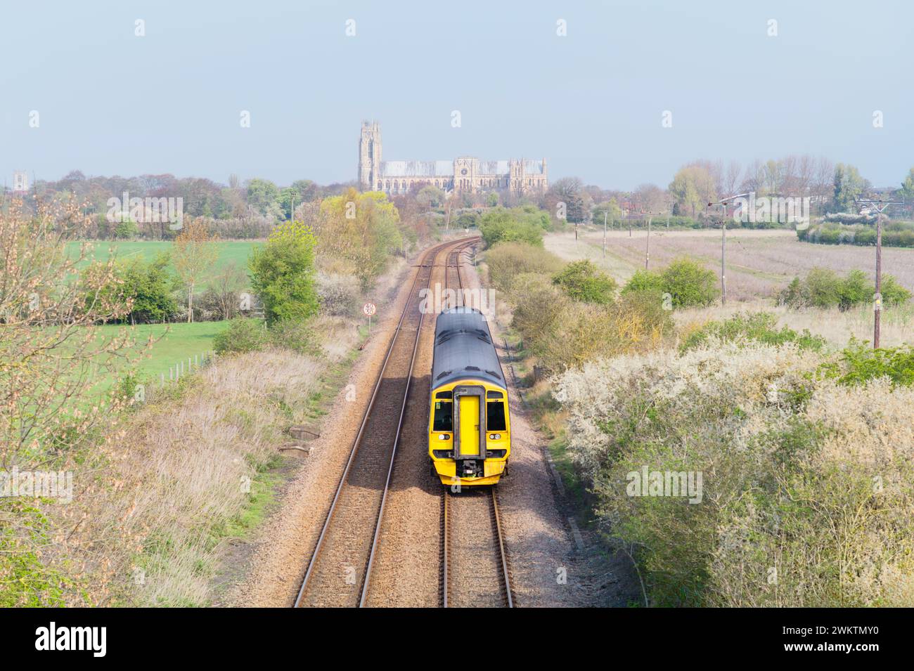 Treno ferroviario fiancheggiato da campi lungo il tragitto per Hull con l'antica minster (chiesa) all'orizzonte, tutto sotto il cielo blu in una bella giornata a Beverley, Regno Unito. Foto Stock