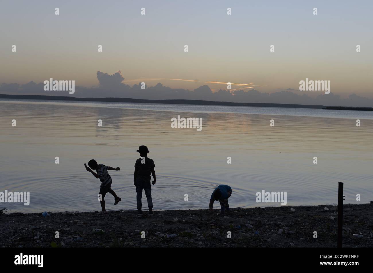 Tre persone in piedi su una spiaggia al tramonto Foto Stock