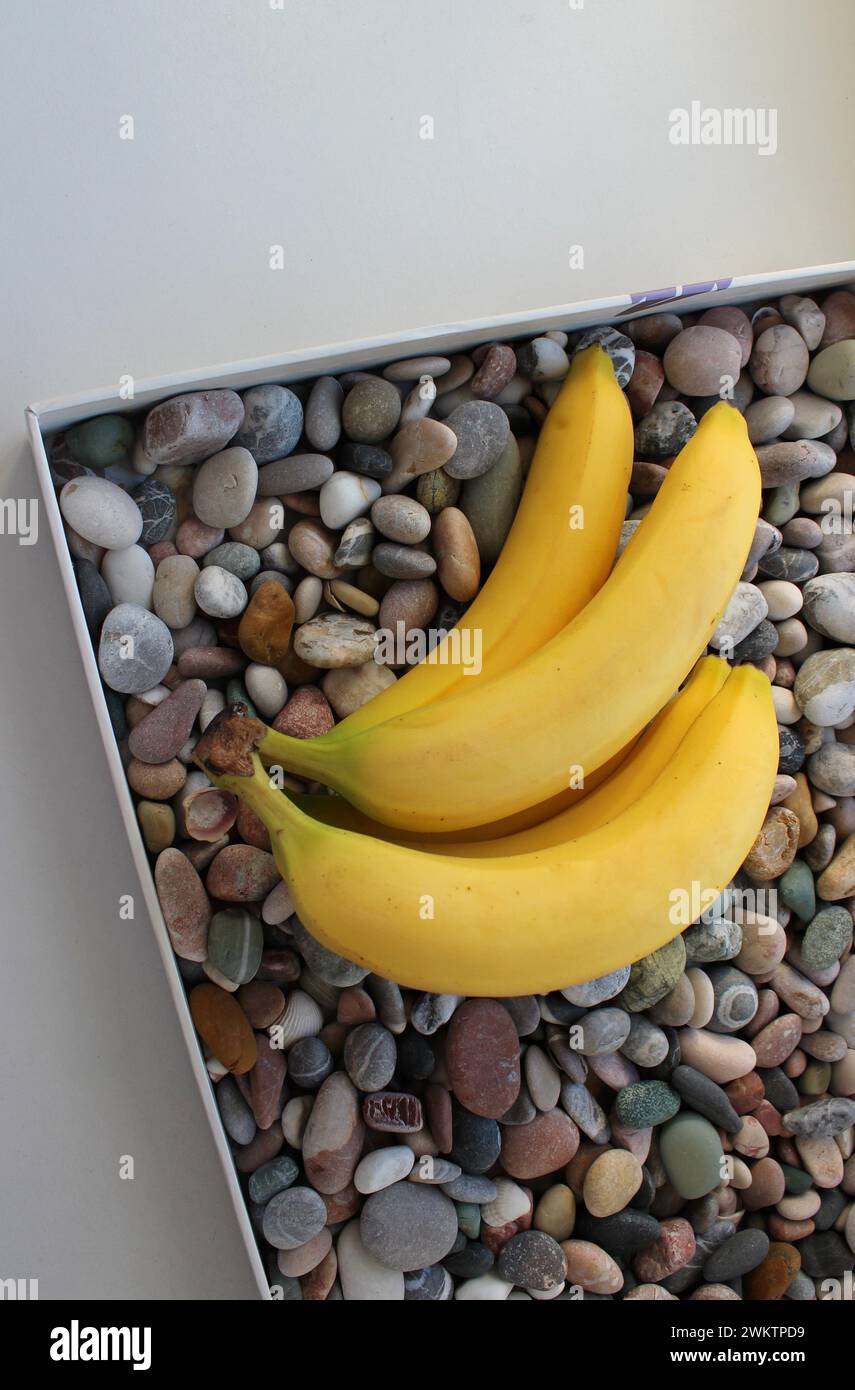 Un mucchio di banane mature su un vassoio con una foto verticale di ciottoli decorativi Foto Stock