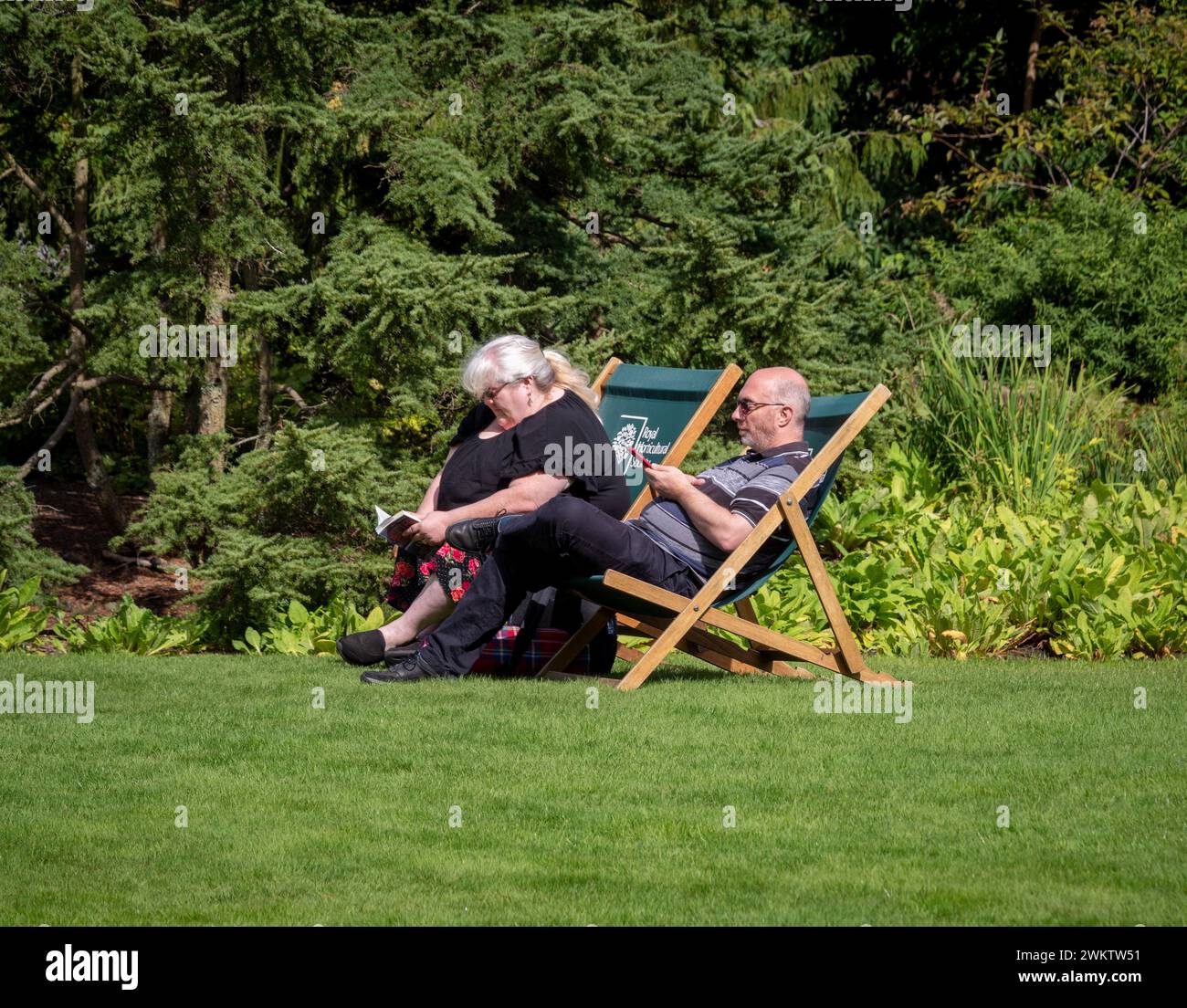 Coppia matura seduta su sedie a sdraio godendosi il sole in un giardino RHS. REGNO UNITO Foto Stock