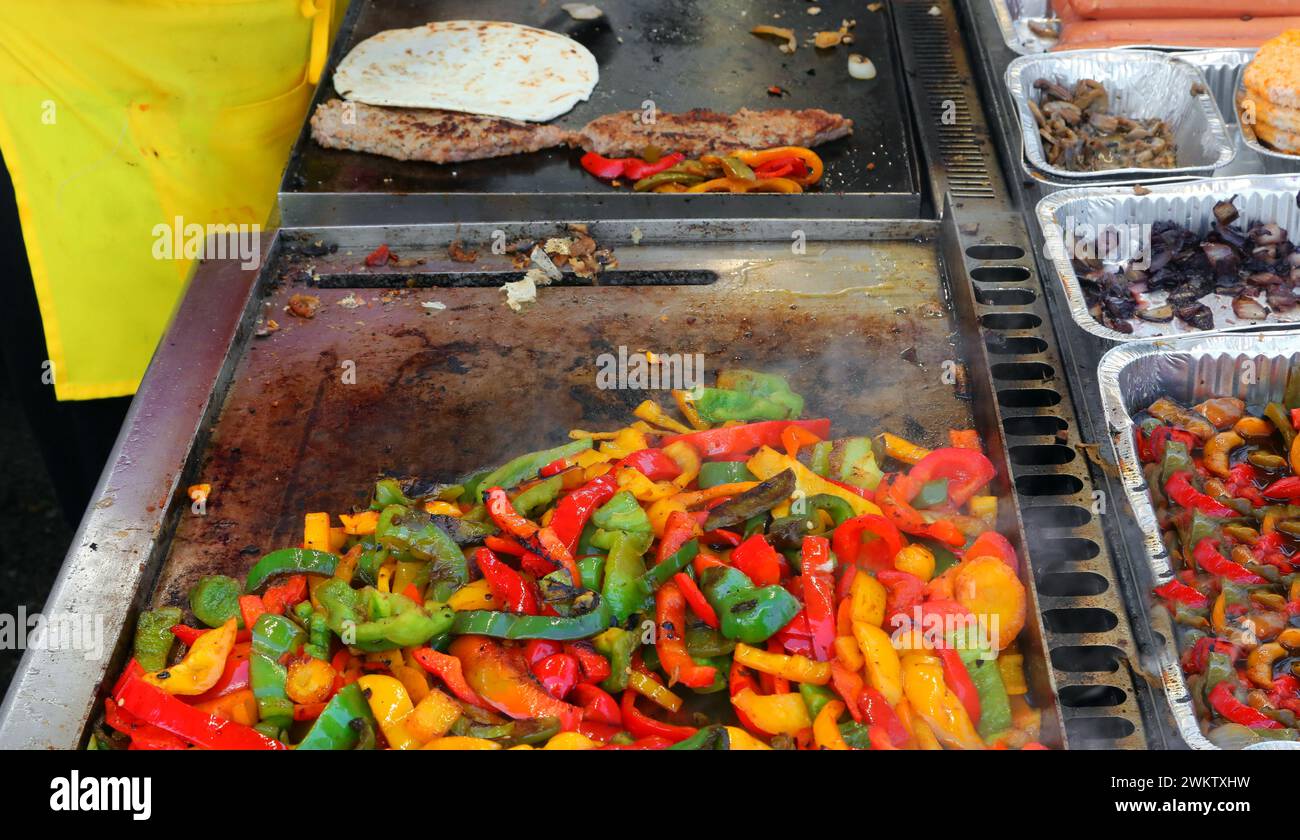 Peperoni gialli rossi e verdi sfrigolanti sulla piastra calda di uno stand di Street food che cucina con le spezie Foto Stock