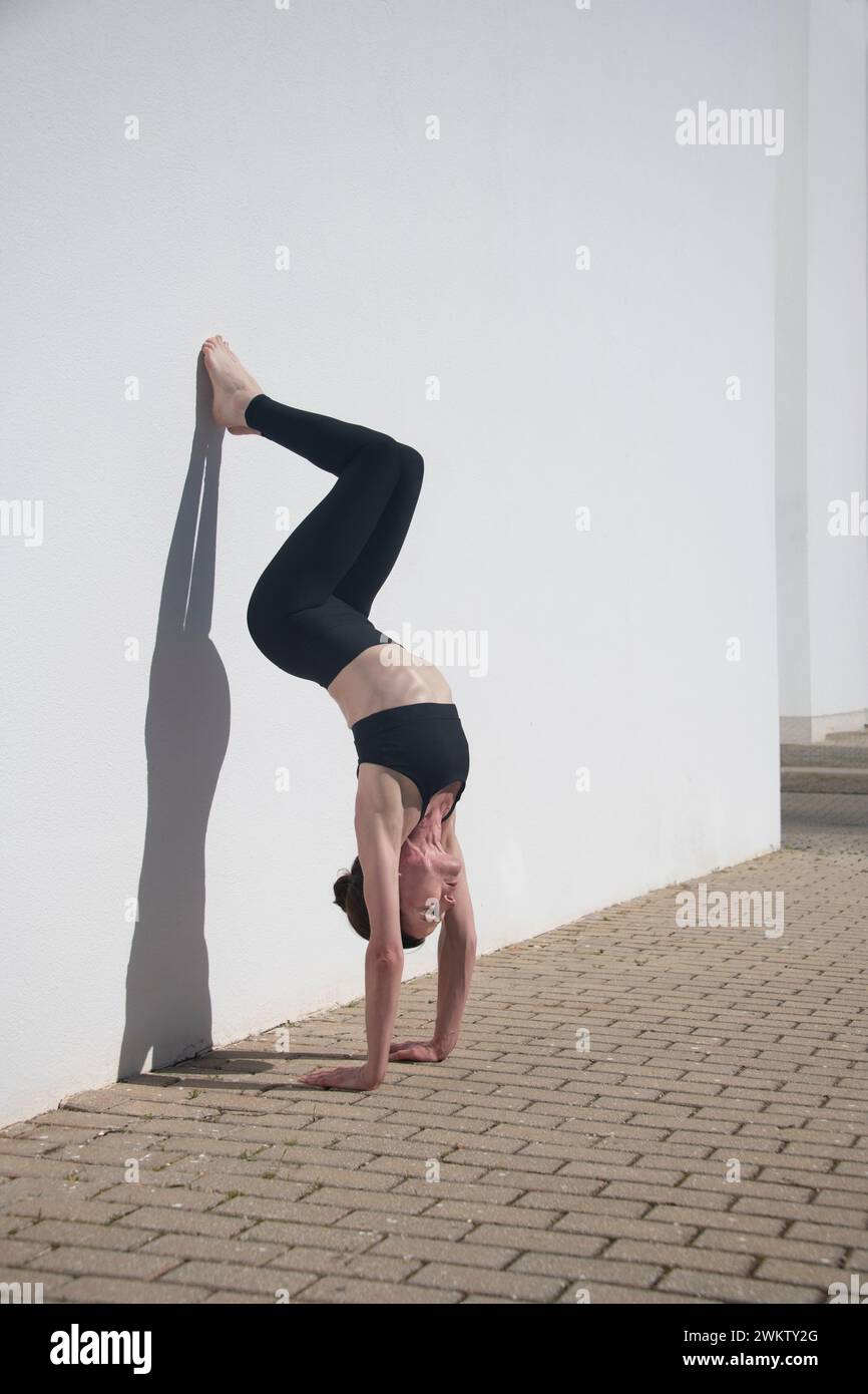 donna che fa una mano contro un muro bianco che costruisce la forza del nucleo, ombre Foto Stock
