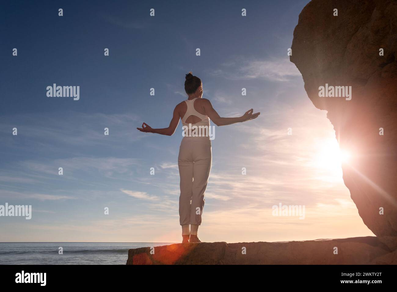 donna in piedi sulle rocce in riva al mare che meditava all'alba Foto Stock