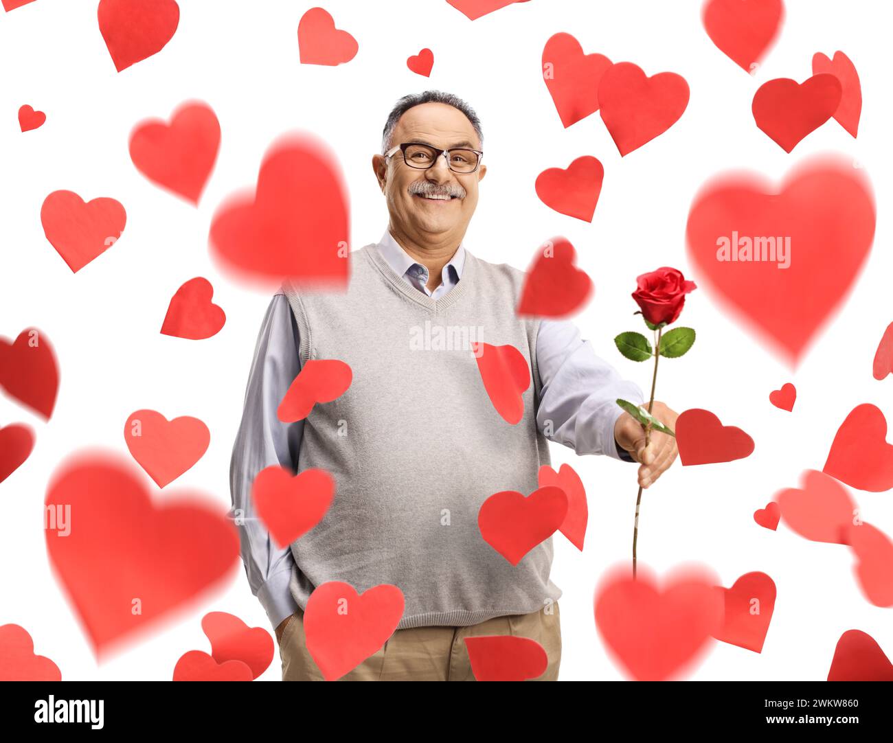 Uomo sorridente maturo che tiene una rosa rossa sotto i cuori cadenti isolato su sfondo bianco Foto Stock